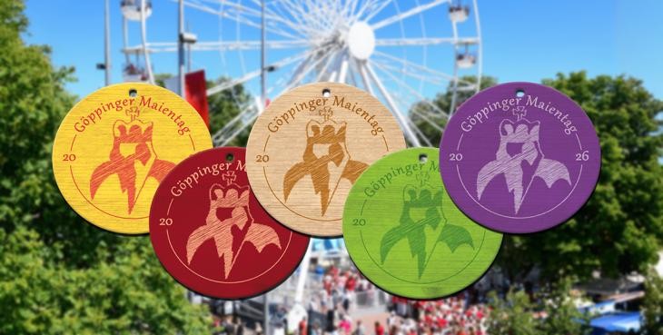 Fünf bunte Maientagsplaketten vor einem unscharfen Riesenrad.