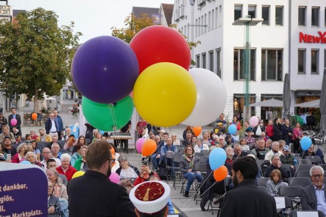 Interkulturelle Wochen in Göppingen Ein Bild mit einem bunten Strauß von Luftballons im Vordergrund, der vom Bürgermeister vor einem Publikum im Freien gehalten wird.
