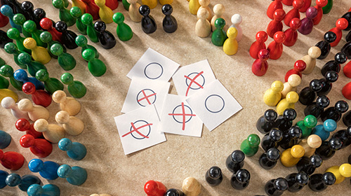 Zahlreiche bunte Spielfiguren stehen um einen Zettel, der einen Wahlschein nachahmen soll.