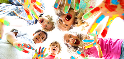 Mehrere Kinder schauen in eine Kamera und halten ihre bemalten Handflächen vor die Linse