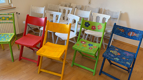 Bunt bemalte Holzstühle stehen in einem Raum.